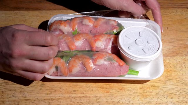 This closeup POV video shows a top view of anonymous hands opening carry out packaging of Vietnamese spring rolls and dipping sauce.