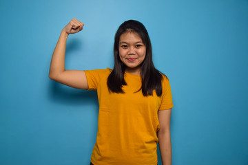 Fototapeta premium Portrait of Young beautiful asian women with blue isolated background, smile and look at the camera,raises arms and shows biceps