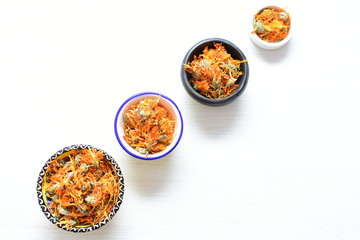 Petals of chopped dried calendula, displayed in containers on white wooden background