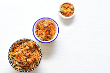 Petals of chopped dried calendula, displayed in containers on white wooden background