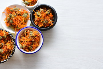 Petals of chopped dried calendula, displayed in containers on white wooden background