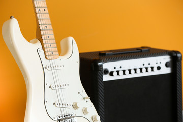 Modern guitar and amplifier on color background