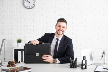 Male lawyer with briefcase sitting at workplace in office