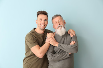 Portrait of senior man and his adult son on color background