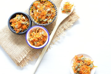 Petals of chopped dried calendula, displayed in containers on white wooden background