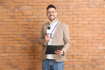 Male journalist with microphone on brick background