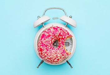 Alarm clock with doughnut on color background