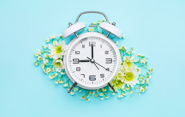 Alarm clock with flowers on color background