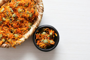 Petals of chopped dried calendula, displayed in containers on white wooden background