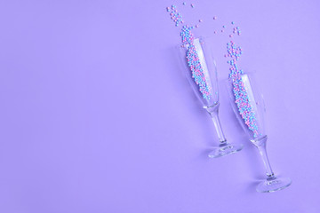 Glasses for champagne with sprinkles on color background