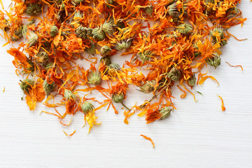 Petals of chopped dried calendula, displayed in containers on white wooden background
