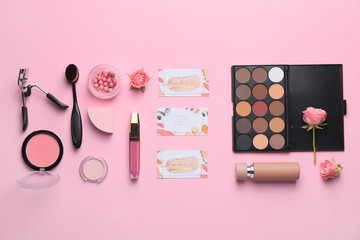 Decorative cosmetics and accessories with business cards of makeup artist on color background