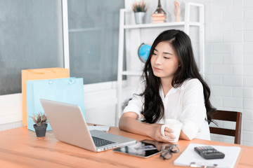 Asian young businesswoman working with new project laptop drinking coffee in coffee shop cafe, Analyze plans, papers, hands writing business plan.design notebook technology  startup business concept