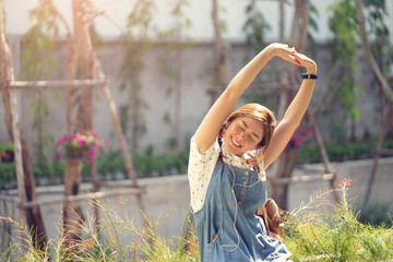 asian woman smiling joyfully and stretching with arms in the air while listening to music with the...