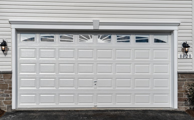 Double car classic insulated steel raised panel garage door framed with a white trim to add accent, with transom light windows divided by muntins on a new American home
