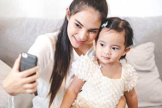 Asian mother are using cell phones take selfie photo with her daughter. The love of a mother with a daughter. Mom and kids, family relationship, child care, technology for children concept.