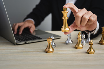 A businessman in a black suit holding chess figure in hand while use laptop. Technology analysis, Business strategy, leadership, management idea, success achievement and organization concept.