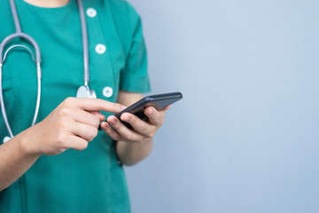 isolated close up body shot of female doctor holding a smart phone with her finger touching the screen, representing technology medical health care, wearing a scrub and a stethoscope around the neck