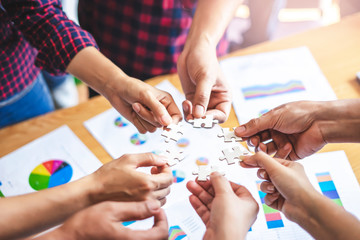  employees standing around in a circle holding jigsaw pieces each matching it against one another, representing teamwork problem solving, help and support within small businesses or company..