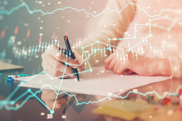 Hand taking notes in notepad. Forex chart holograms in front. Concept of research. Multi exposure