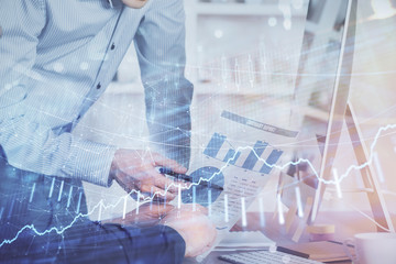 Double exposure of chart with businessman typing on computer in office on background. Concept of hard work.