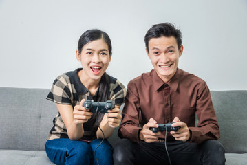 Young asian couple in love and playing video games holding joystick while sitting on sofa in living...
