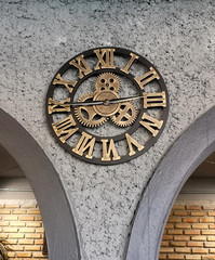 The beautiful design clock shows a golden gear hanging on a wall covered in gray.