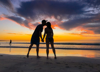 Silhouettes of couple in love kissing at beach sunset celebrating freedom and love