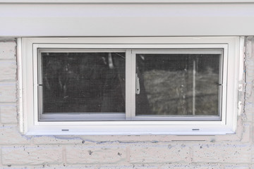 Basement sliding window with thick white frame on a newly constructed American home, slider with stationary sash and one that slides open horizontally