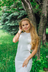 Portrait of a charming blond woman wearing beautiful white dress standing next to rowan tree.