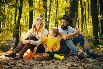 Happy family of three lying in the grass in autumn. A young family with small child having picnic in autumn nature at sunset. Mother, bearded father and kid are eating apples.