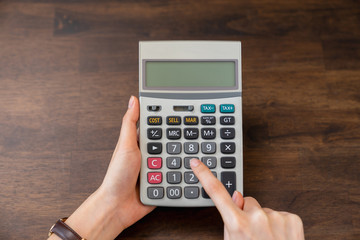 Close-up of hand holding calculator on wood table.