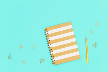 Top view of working table with closed copybook on spring, yellow colored pencil,  golden metal clips for paper and documents. Flat lay with stationery for school, education.