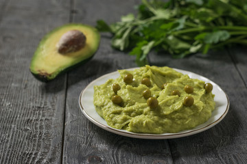 Guacamole with green peas and half an avocado with parsley leaves on a wooden table. Diet vegetarian Mexican food avocado.