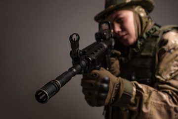 Portrait of  soldier in military camouflage uniform protected with helmet, body armour, holding machine gun desaturated on a gray background.