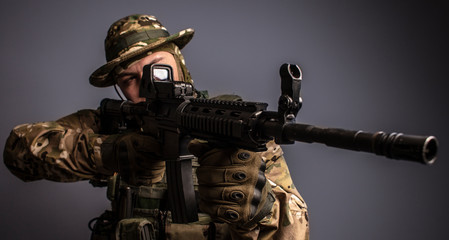 Portrait of  soldier in military camouflage uniform protected with helmet, body armour, holding machine gun desaturated on a gray background. War, warrior.