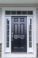 Classic fiberglass prehung black front door, raised panels, white frame, sill, jamb separating the divided sidelights, transom windows separated by narrow white grilles