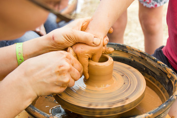 A close up view on ceramic production process on potter's wheel with children. Clay crafts with kids concept.