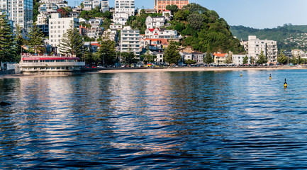 Oriental Bay beach in Wellington, NZ with buildings reflected in the sea on a calm summer's morning.