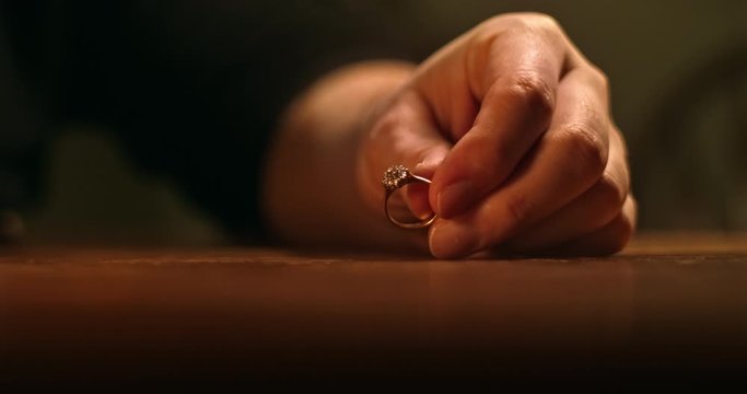 Cinematic close up of recently divorced, unhappy man looking at wedding ring in hand