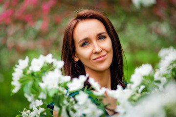 Naklejka premium beautiful young brunette woman standing near the apple tree on a warm summer day