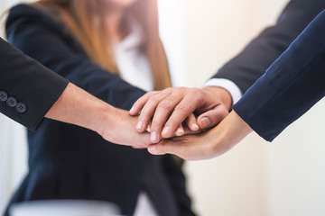 Obraz premium asian businessmen and businesswomen putting hands together piling on top of one another representing teamwork, community, help and support within the business or company within an office environment