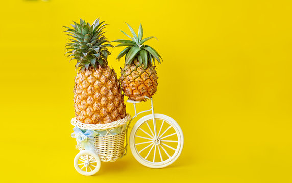 Two pineapples on a bicycle on a yellow background. Space for text