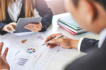 close up of a businesswoman and businessman working together in an office, using tablet device, books, notebook and pen pointing at the work of statistics, charts and graphs on the paper documents