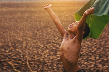 Climate change, Asian boys enjoy with first falling rain season on dry cracked land. Environment...