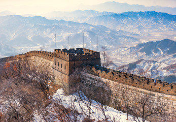 The great wall china in the wintertime with snow on the mountain.