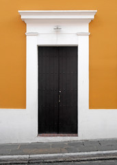 Fototapeta na wymiar Weathered wooden doors set into an orange wall with white wooden trim along cobblestone sidewalk in old town San Juan.