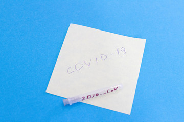 Paper sticker with text COVID-19 and needle test tube. Novel virus nCov-2019 on blue background