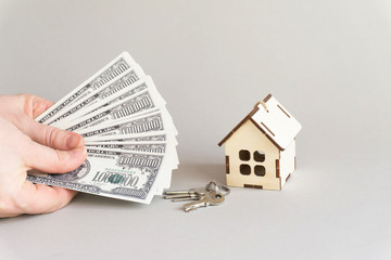 Women's hands count money in dollars against the background of a miniature house and metal keys. Grey isolated background, copy space. The concept of business and Finance, real estate acquisition.