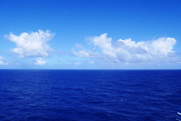 Fototapeta premium Soft white clouds pass over the calm cobalt blue waters of the Caribbean Sea as seen from the deck of a cruise ship.